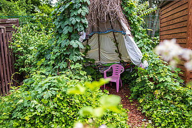 Tipi im Schrebergarten mit einem lilafarbenen Plastik-Kinderstuhl
