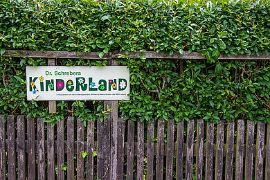 Hecke und Holzzaun und ein Schild mit der Aufschrift "Dr. Schreibers Kinderland"