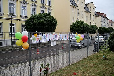 Am Tor der Kita hängt der Schriftzug Herzlich Willkommen. Die einzelnen Buchstaben wurden von den Kindern bunt ausgemalt.