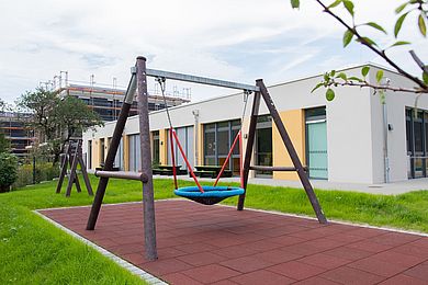 Eine Nestschaukel steht im Garten der Kita für die spielenden Kinder bereit.