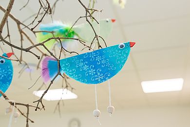 Ein selbst gebastelter Vogel aus glitzerndem Velourpapier hängt als Dekoration an einem Strauß aus Zweigen.