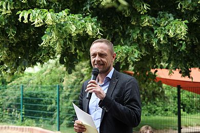 Hauptgeschäftsführer Tobias Schmidt gratuliert der Leitung und dem Team der Kita Gerne Groß mit einer kleinen Ansprache zum Jubiläum. Dabei trägt er ein hellblaues Hemd und ein graues Sakko.
