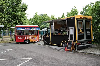 Vor der Kita stehen zwei Foodtrucks, die Softeis und Burger anbieten.