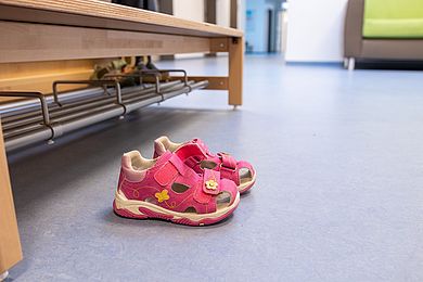 Zwei rosafarbene Kindersandalen stehen vor einer Holzbank in der Garderobe.