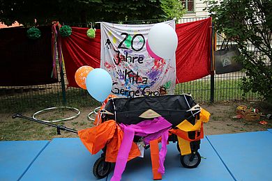 Der Bürgermeister von Markkleeberg nimmt das Jubiläum zum Anlass, um der Kita einen Bollerwagen zu schenken. Auf dem Bild steht dieser dekoriert mit Luftballons vor dem Transparent 20 Jahre Gerne Groß.