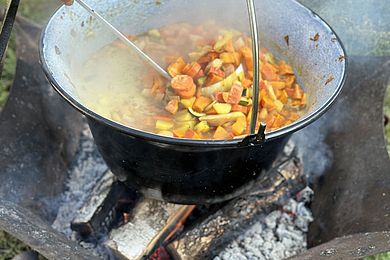 In einem großen Topf köcheln über einer Feuerschale Möhren, Kartoffeln und Kürbis. 