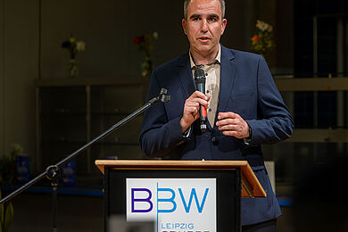 Martin Fünftück von Siemens Compressors Energy am Rednerpult. Er hält das Mikrofon in der rechten Hand. Auf dem Rednerpult ist das Logo der BBW-Leipzig-Gruppe zu sehen. Er trägt einen dunkelblauen Anzug.