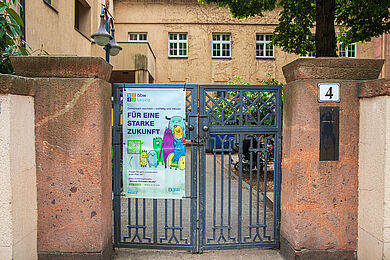 Tor zur Willmar-Schwabe-Straße 4, ein rötliches Sandsteingebäude. Am Tor hängt ein Plakat der BBW-Kitas mit der Aufschrift "Für eine starke Zukunft"