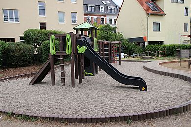 Das Zentrum des Gartens ist ein Spielbereich mit braunem Klettergerüst und Rutsche.
