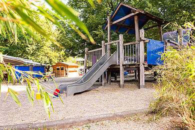 Großes Klettergerüst im Sandkasten, außenrum Bäume und Büsche