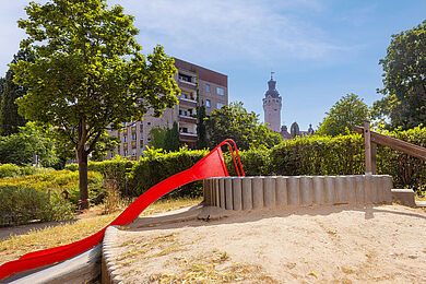 Rutschhügel im Garten der Kita mit Sandkasten, im Hintergrund der Turm des Neuen Rathauses